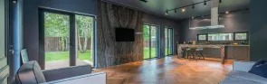 A modern kitchen and living room featuring large windows that allow natural light to fill the space.